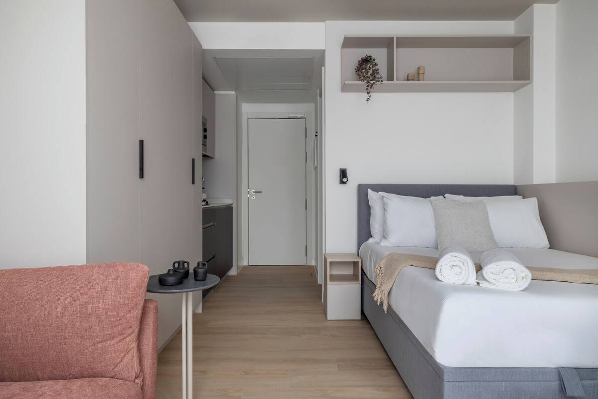A modern bedroom with a bed, a small table with a chair, and a wardrobe.