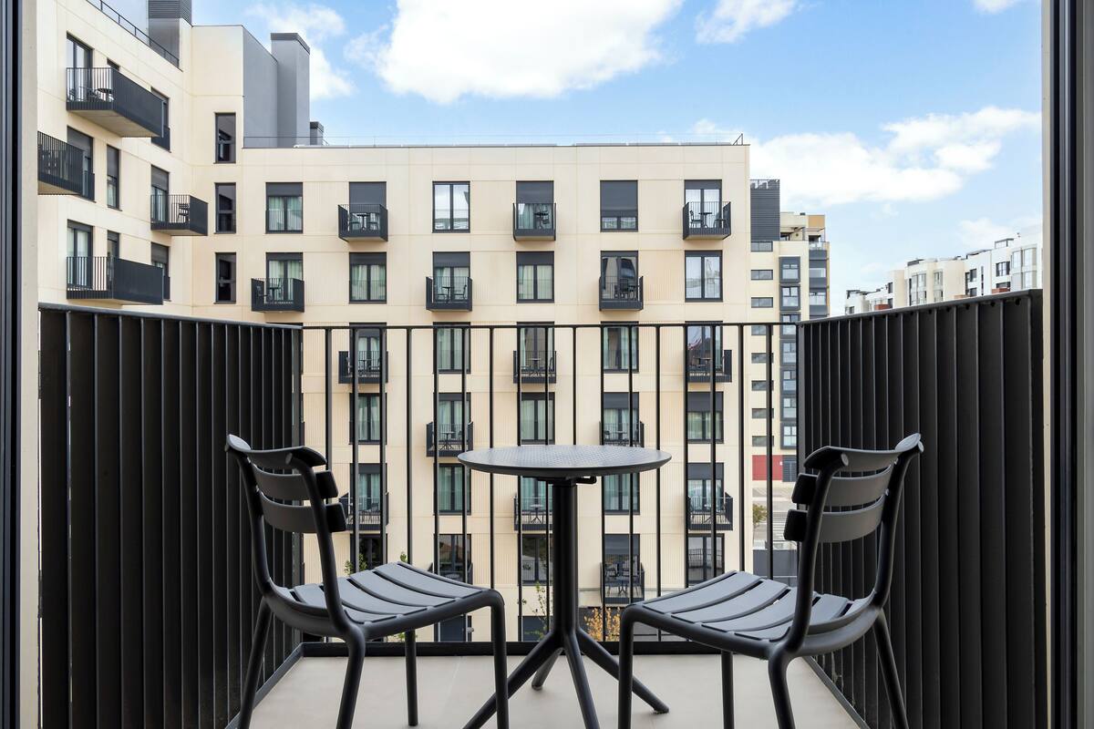 A balcony with two chairs and a small round table, overlooking a building with multiple balconies and windows.