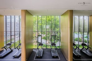 Ein modernes Fitnessstudio mit Laufbändern vor großen Fenstern, die einen Blick auf eine Straße und Grünflächen bieten.