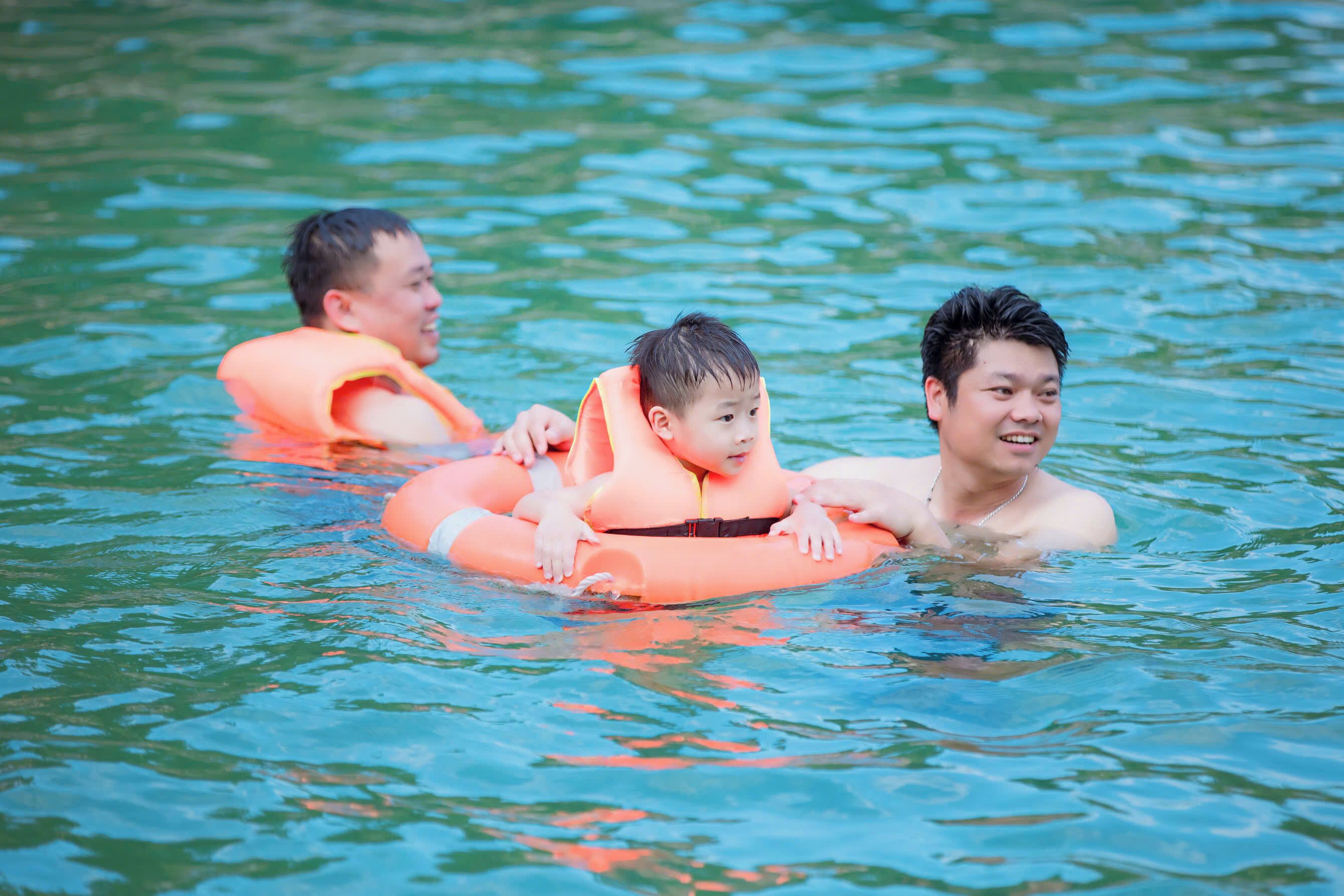Three people in a body of water, each wearing an orange life jacket.
