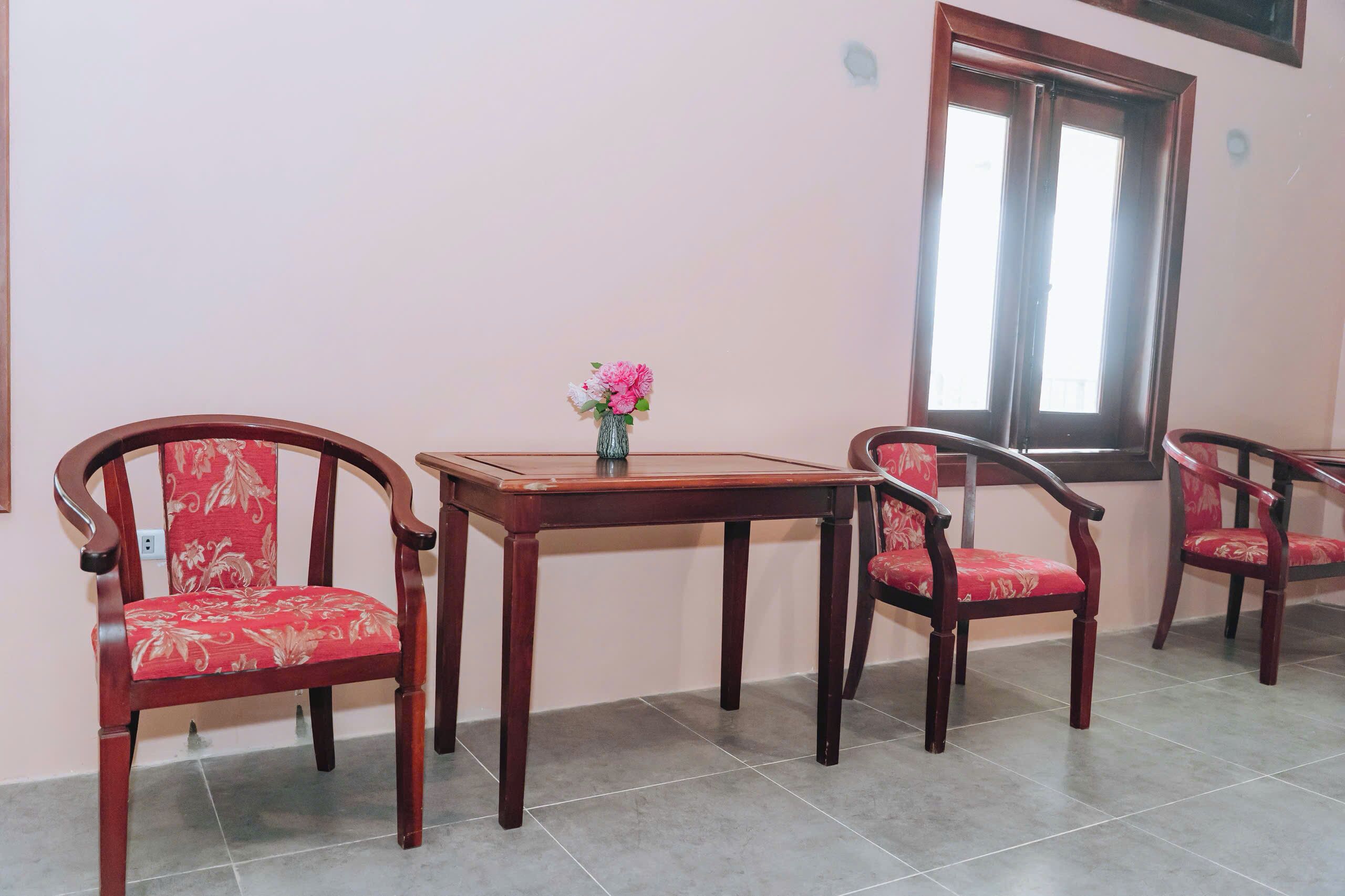 A room with a wooden table and four chairs, a vase with flowers, and a window.