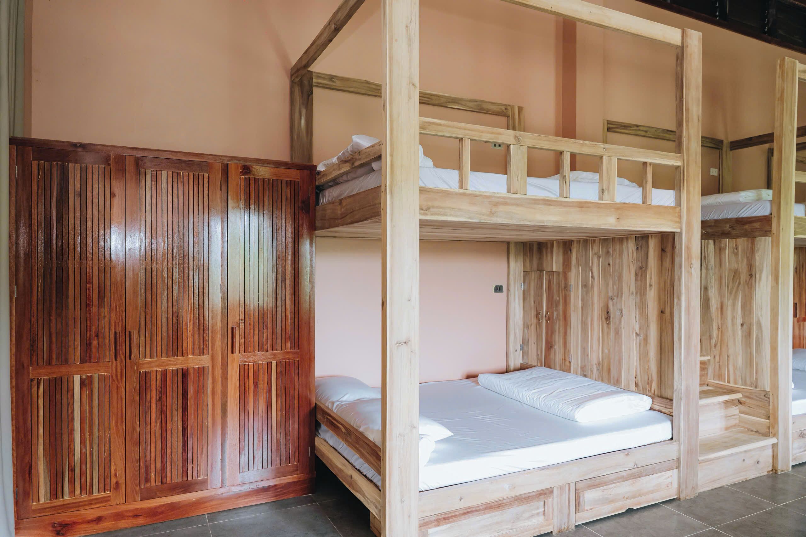 A room with two bunk beds, wooden wardrobe, and a tiled floor.
