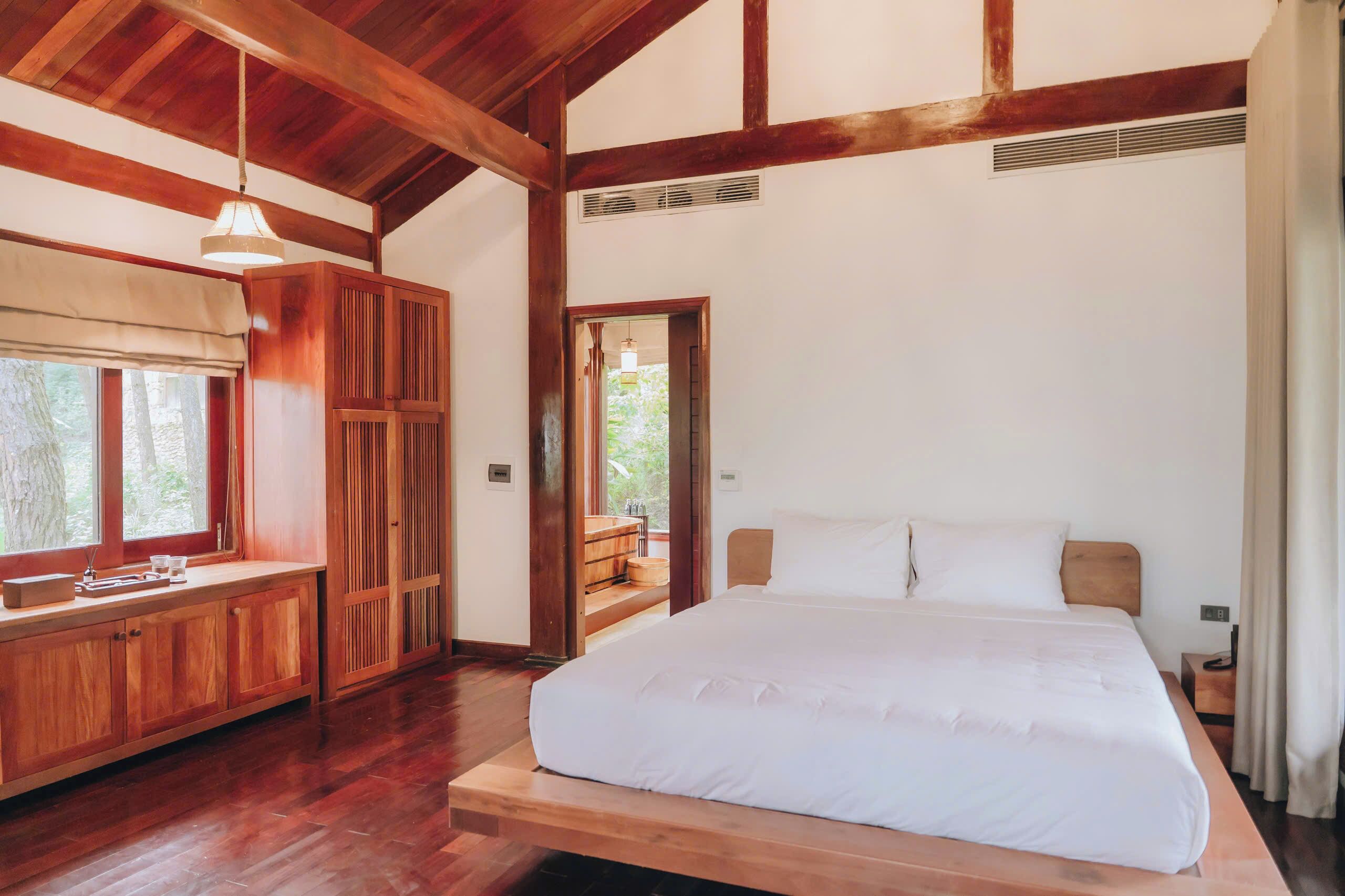 A wooden-framed bedroom with a large bed, a wooden bench with a window, and a door leading to an outdoor area.