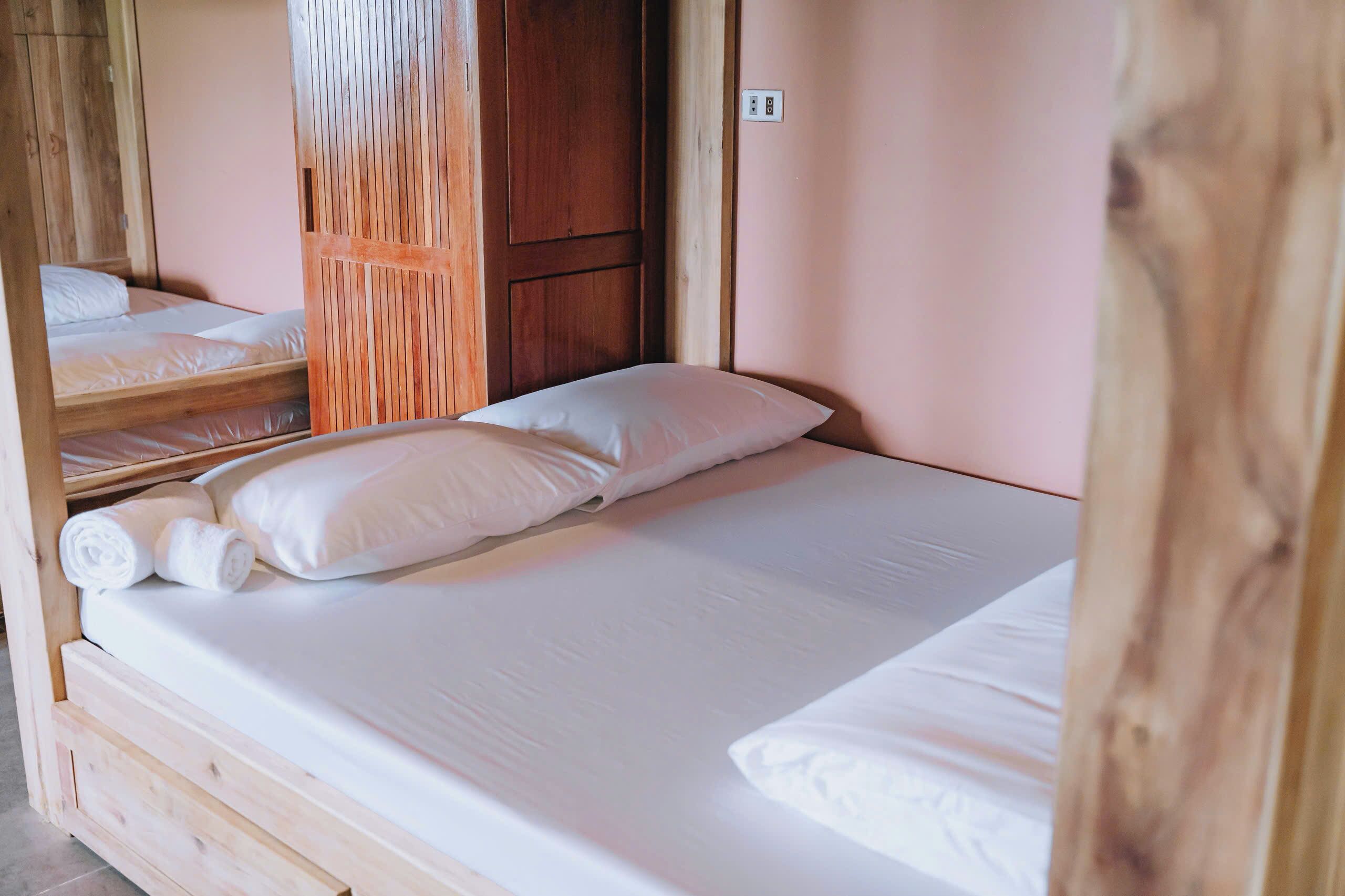 A single bed with white linens and pillows, a wooden headboard, and a wooden partition wall.