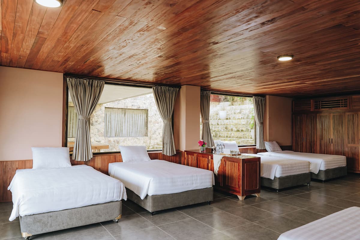 A hotel room with three beds, wooden ceiling, stone walls, and large windows with curtains.