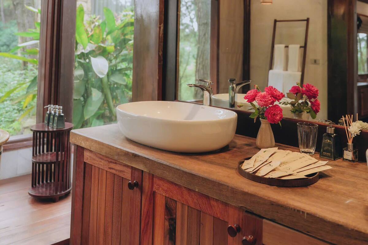 A wooden vanity with a large sink, a mirror, and a vase with red flowers.