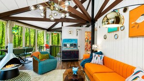A spacious living area with a large orange sofa, a teal armchair, and a wooden ceiling with exposed beams.