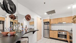 A modern kitchen with a central island, stainless steel appliances, and wooden cabinets. - Beachside Studio With Pool and Gym Access (Sydney)