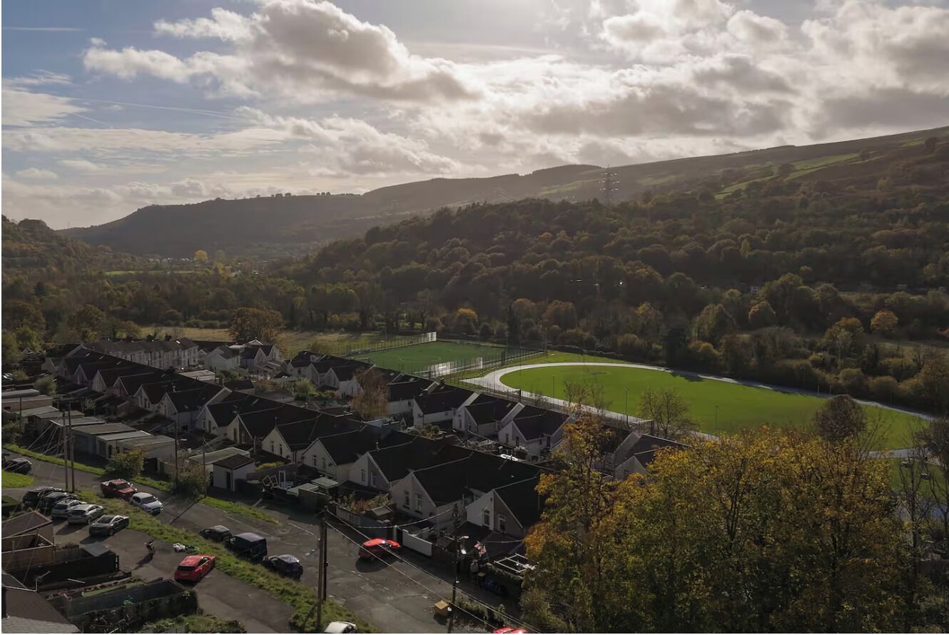 Un quartier résidentiel avec des maisons, un champ verdoyant et une colline en arrière-plan.