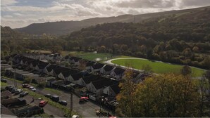 A residential area with houses, a green field, and a hill in the background. - Stylish & Spacious Retreat in Troedyrhiw | Sleeps 6 | Garden Decking (Troedyrhiw)