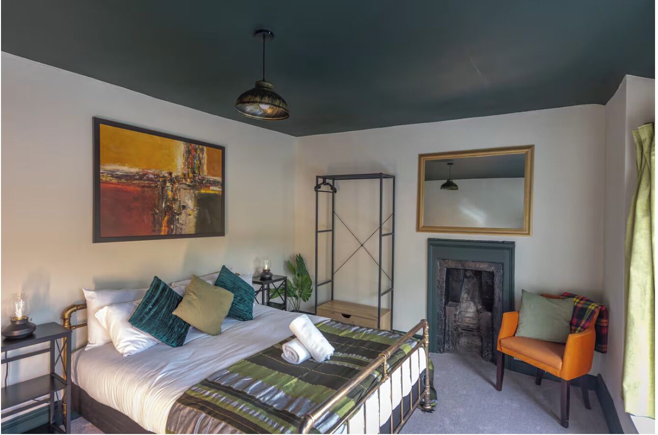 Une chambre à coucher avec un lit, un tableau, une cheminée, une chaise et un miroir.
