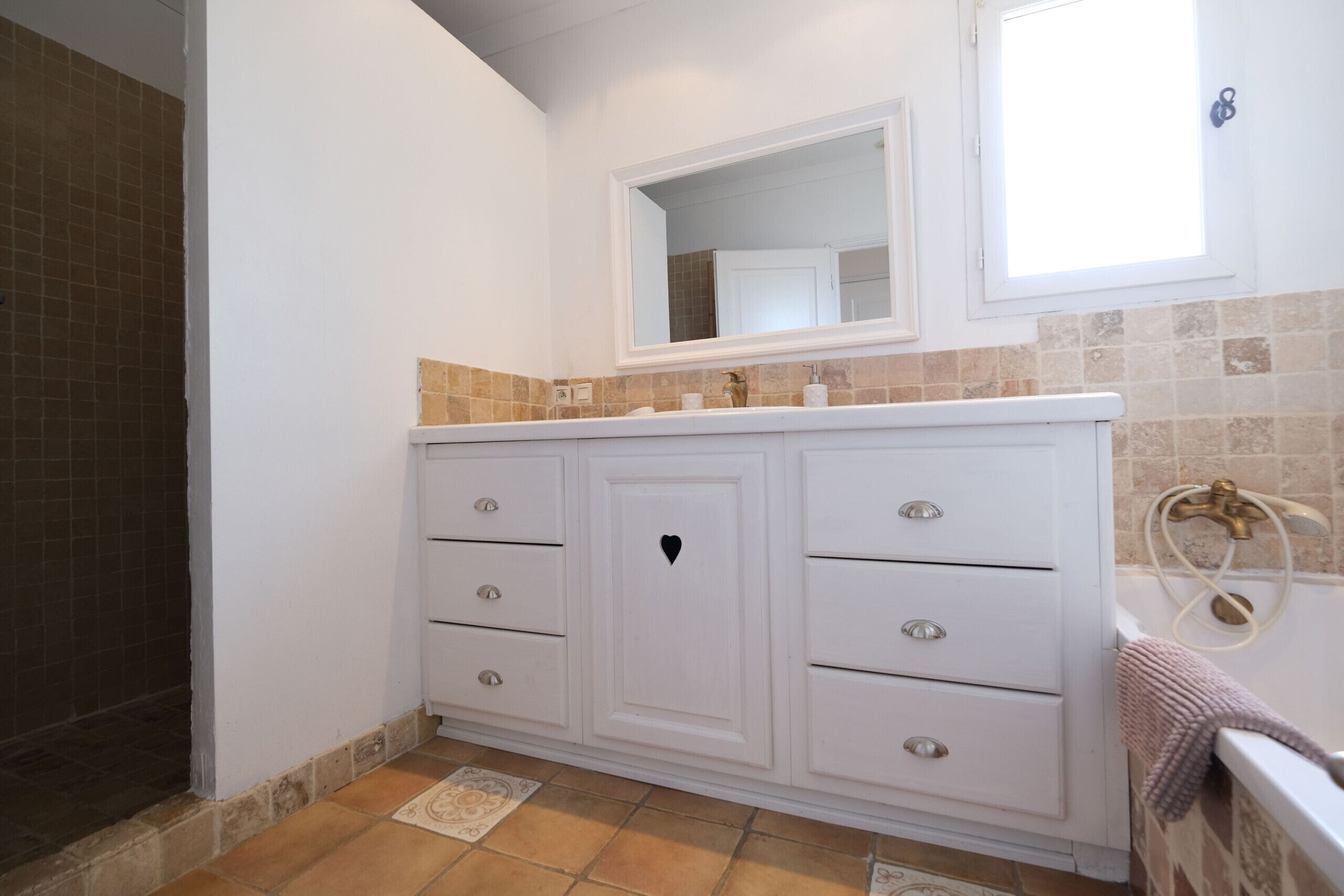 A bathroom with a white vanity, a mirror, a towel rack, and a shower area.
