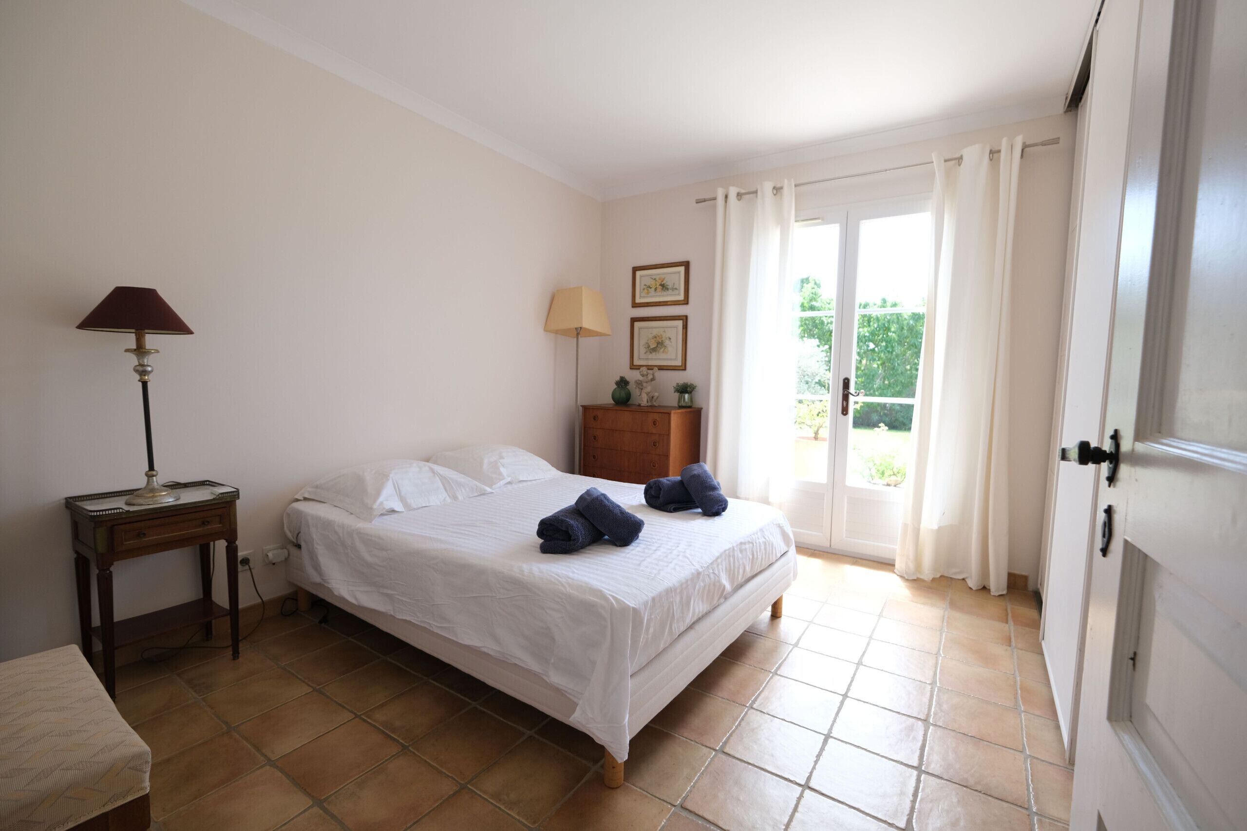 Ein Schlafzimmer mit einem Bett, zwei Nachttischen, einer Kommode, einem Fenster mit Vorhängen und einer Tür.