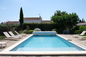 Una piscina rectangular con un deck blanco, rodeada de sillas de descanso y un seto.