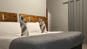 A neatly made bed with a patterned blanket and pillows, a wooden headboard, and a curtain on the window.