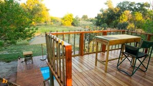 A wooden deck with a table and chairs, overlooking a natural landscape.