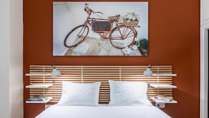 Une chambre à coucher avec une tête de lit en bois, du linge de lit blanc et un tableau représentant un vélo accroché au mur.