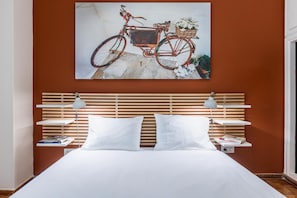 Ein Schlafzimmer mit einem hölzernen Kopfteil, weißer Bettwäsche und einem Wandbild eines Fahrrads.