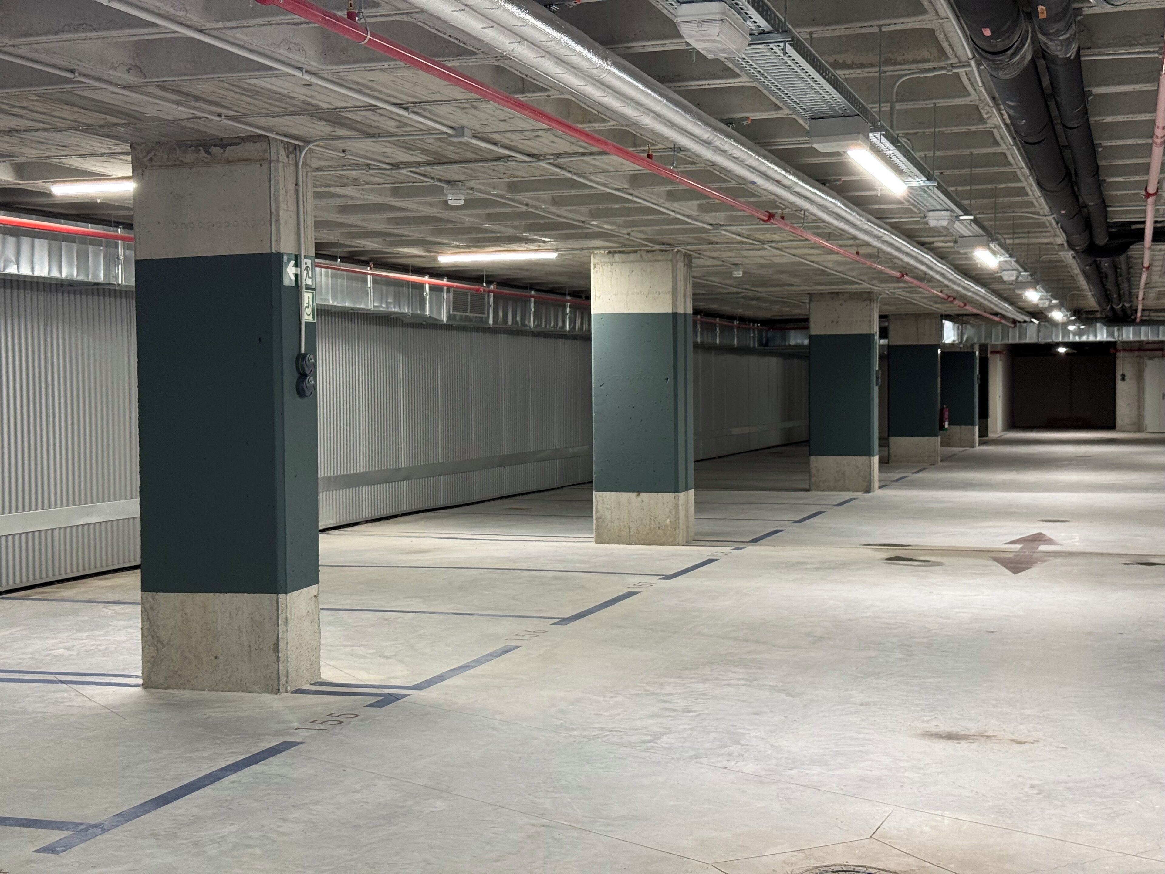 Un parcheggio pulito e vuoto, con pilastri in cemento e tubazioni a soffitto.