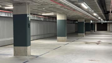 Un estacionamiento limpio y vacío con pilares de hormigón y tuberías en el techo.