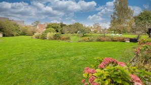 A well-maintained garden with a variety of plants and trees, a clear sky, and a distant view of buildings. - Tenda room (Douzy)
