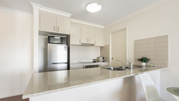 A modern kitchen with white cabinets, a stainless steel refrigerator, a granite countertop, and a sink. - Relaxed 2br, 2bth Apartment With Balcony & Parking (Canberra)