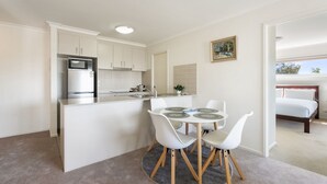 A modern kitchen with white cabinetry, a built-in microwave, and a dining area with a round table and white chairs. - Relaxed 2br, 2bth Apartment With Balcony & Parking (Canberra)