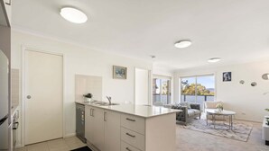 A modern kitchen with white cabinets, a central island, and a dishwasher. There is a dining area with a sofa and a small table. - Relaxed 2br, 2bth Apartment With Balcony & Parking (Canberra)