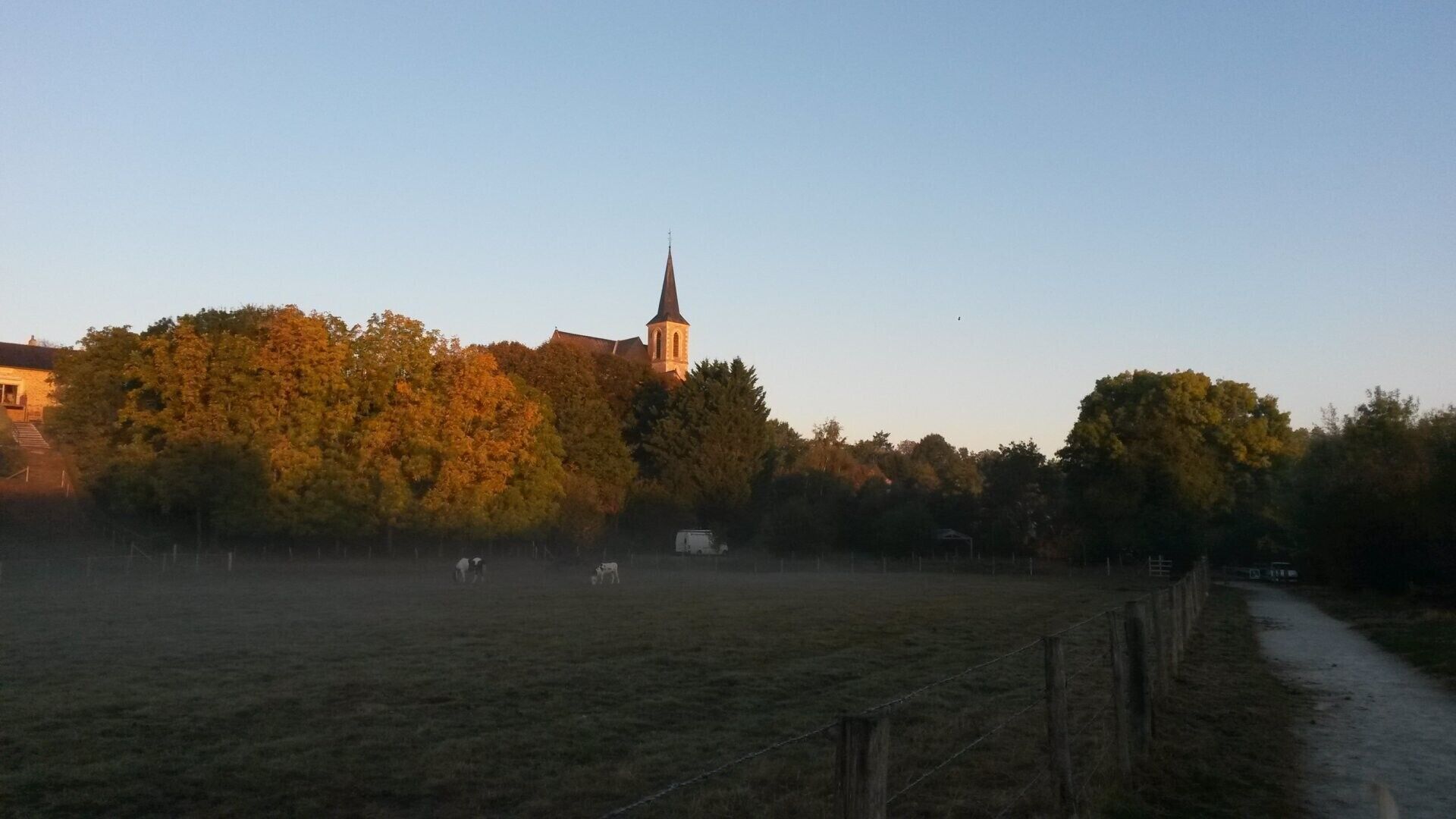 A rural landscape with a church, open fields, and a fence.