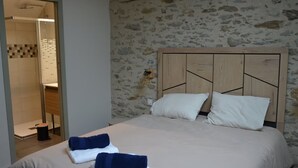 A bedroom with a stone wall, a wooden headboard, and a bed with white bedding and blue towels. - Bed and Breakfast 'L'Isle Briand' with Wi-Fi (Montreuil-sur-Maine)