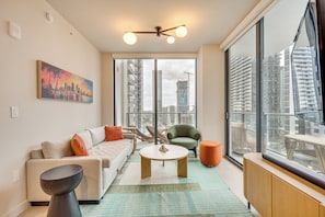 A modern living room with a sofa, coffee table, armchair, and a large window offering a city view. - Summer-ready Miami High-rise w/ Biscayne Bay Views (Miami)
