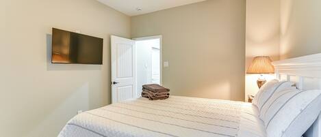A bedroom with a bed, a flat-screen TV mounted on the wall, a ceiling fan, and a door leading to another room.