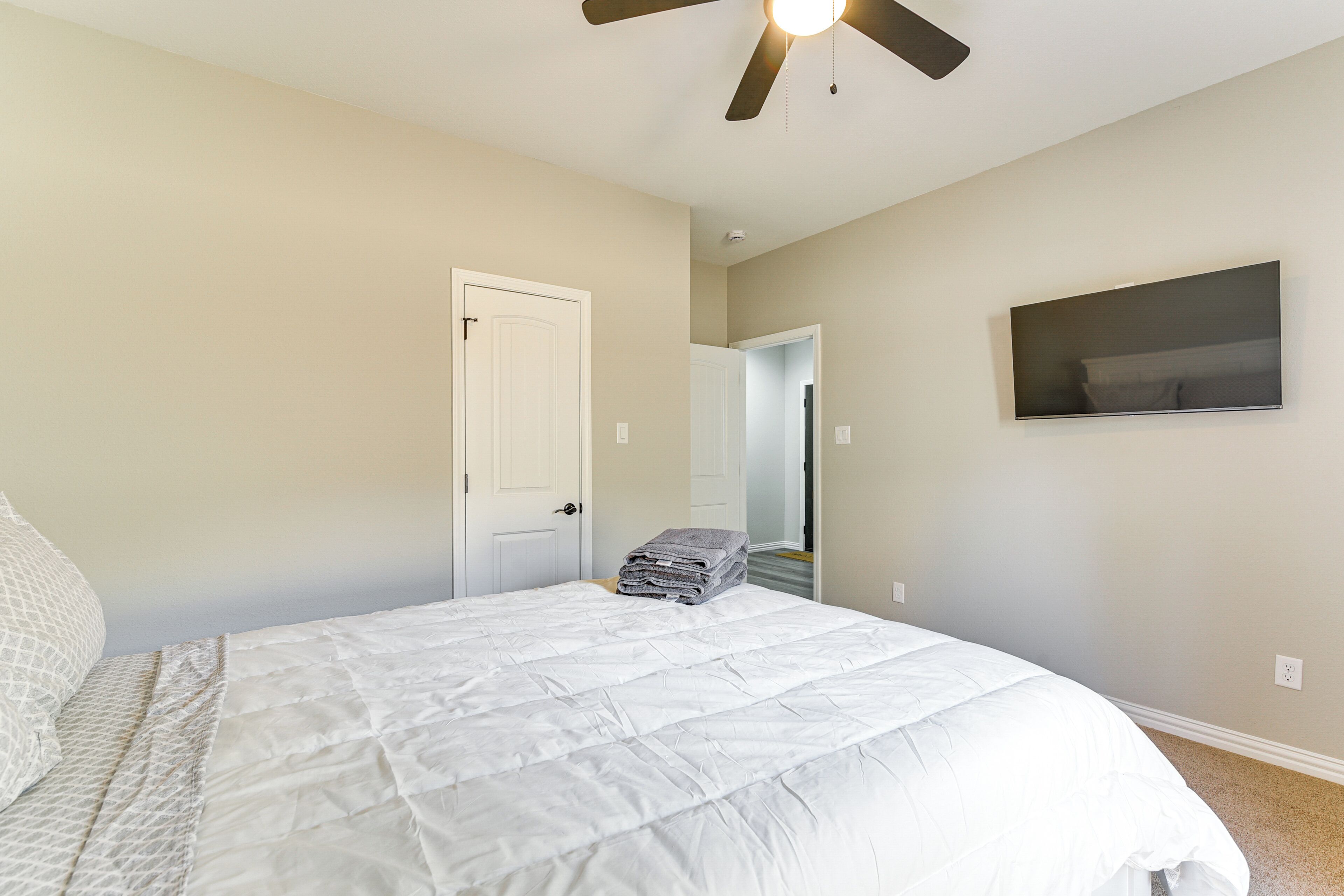 Une chambre à coucher avec un lit, un ventilateur de plafond, une porte et un téléviseur fixé au mur.