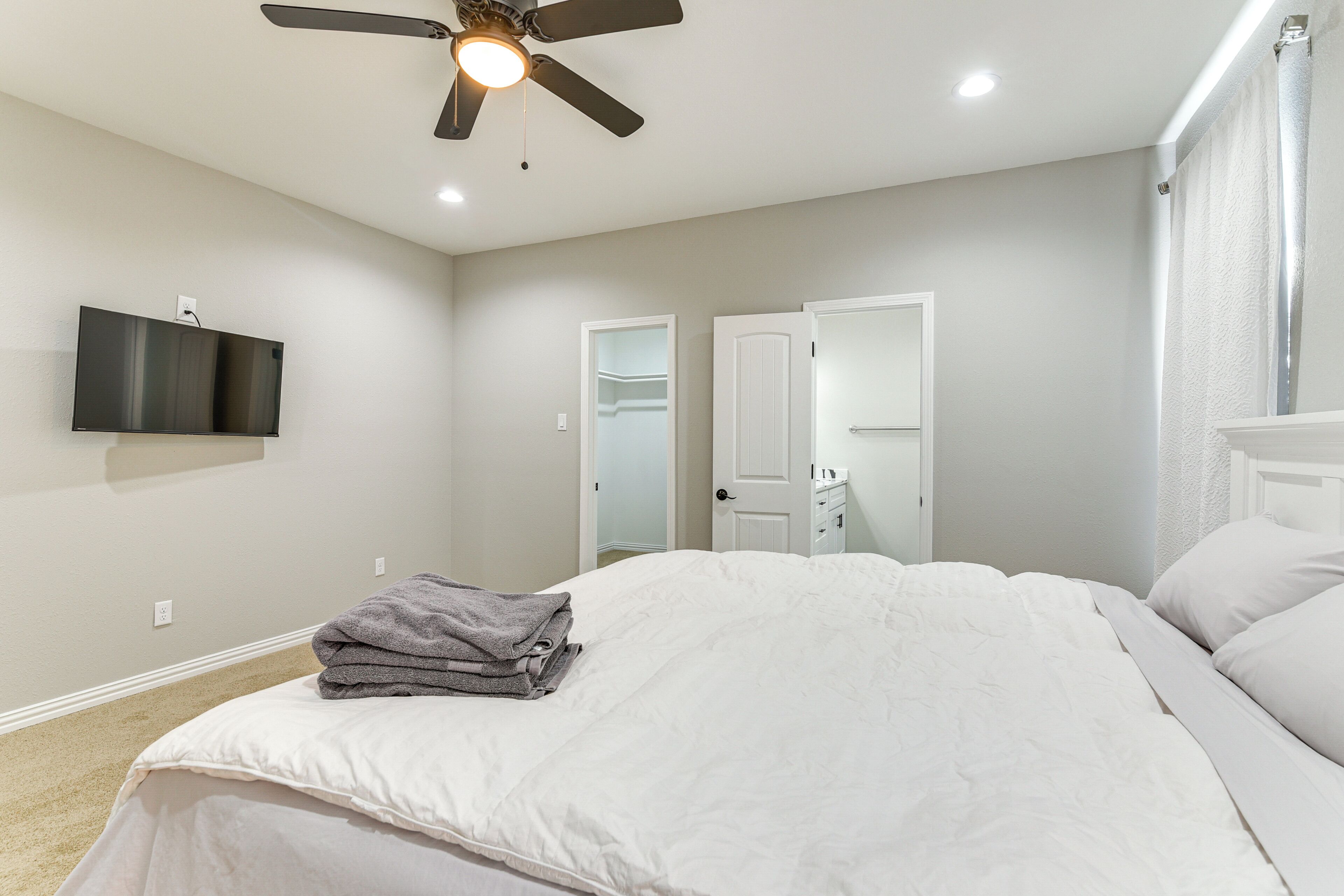 A bedroom with a bed, a ceiling fan, a TV mounted on the wall, and a closet with a mirror.