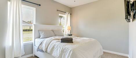 A bedroom with a bed, a ceiling fan, a window with curtains, a lamp, and a TV mounted on the wall.