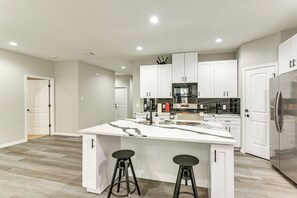 A modern kitchen with white cabinetry, a central island with stools, and built-in appliances. - Easy Hwy Access to Dtwn: Pet-friendly Houston Home (Houston)