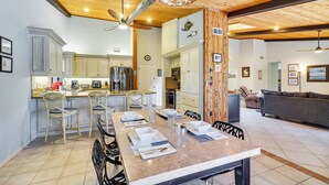 Une cuisine moderne avec des meubles en bois, un coin repas avec une table dressée pour quatre personnes, et un salon avec un canapé et une cheminée.