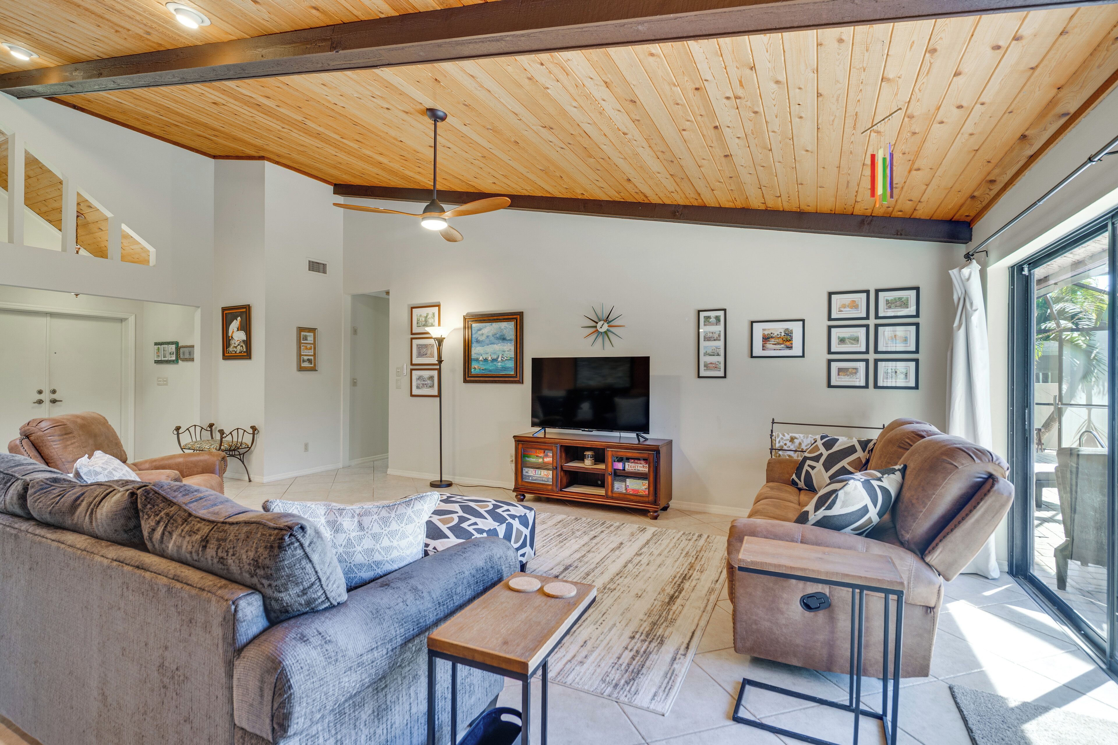 A spacious living room with a high ceiling, a television, and a large window providing a view of the outdoors.