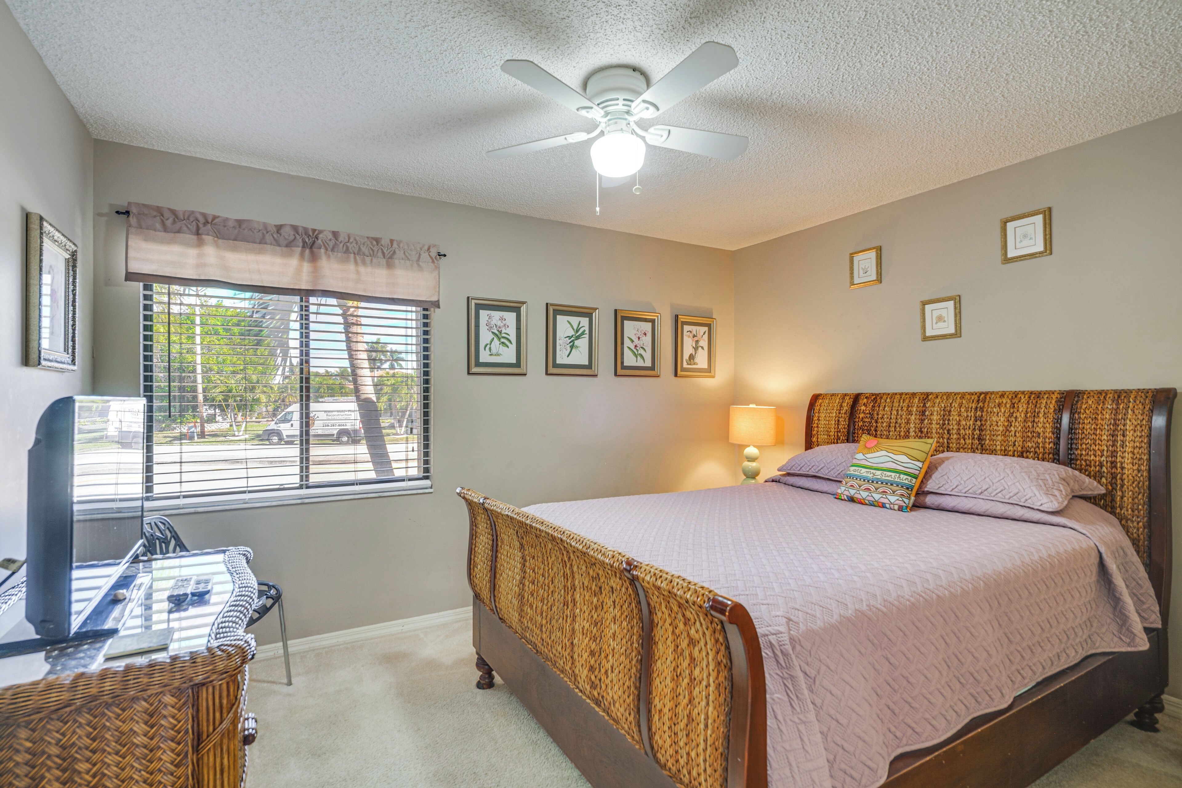 A bedroom with a bed, a desk, a chair, a ceiling fan, and a window with blinds.