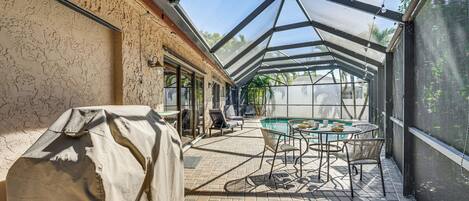 A covered patio with a pool table, chairs, and a grill.