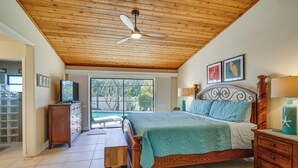 Une chambre avec un plafond en bois, un lit recouvert d’une courtepointe bleue, une table de chevet en bois, une commode en bois et un ventilateur de plafond.