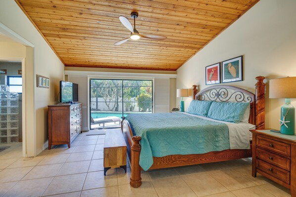 A bedroom with a wooden ceiling, a bed with a blue bedspread, a wooden nightstand, a wooden dresser, and a ceiling fan. - Heated Pool, 3 Mi to Dtwn: Cape Coral Escape! (Cape Coral)