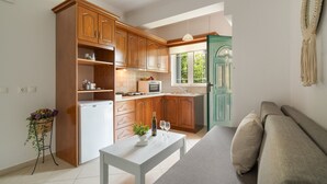 A compact kitchen with wooden cabinets, a white refrigerator, a dining table with a bottle and glasses, and a green door leading outside. - Anna's One-Bedroom Apartment with Balcony, Wi-Fi and Air Conditioning (Νικιάνα)