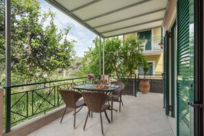 Ein Balkon mit Korbstühlen, einem Tisch mit einer Speisenplatte und einem Blumentopf.