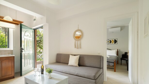 A living room with a sofa, a coffee table, a mirror, and a dining area with a chair. - Anna's One-Bedroom Apartment with Balcony, Wi-Fi and Air Conditioning (Νικιάνα)