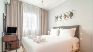 A hotel room with a bed, a desk with a TV, and a window with curtains. - Anna's Two-Bedroom Apartment with Mountain View, Wi-Fi, and Air Conditioning (Νικιάνα)