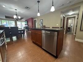 Cozinha com ilha central, máquina de lavar louça em aço inoxidável e iluminação pendente.