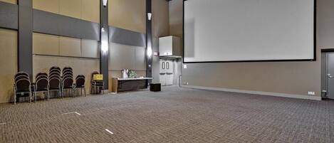 A large conference room with a carpeted floor, a projection screen, a podium, and several chairs arranged in a row.