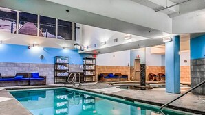 A modern indoor pool area with a clear pool, blue seating, and a staircase leading to upper levels. - Solara 2BR Retreat Pool- Hot Tub -113 (Canmore)