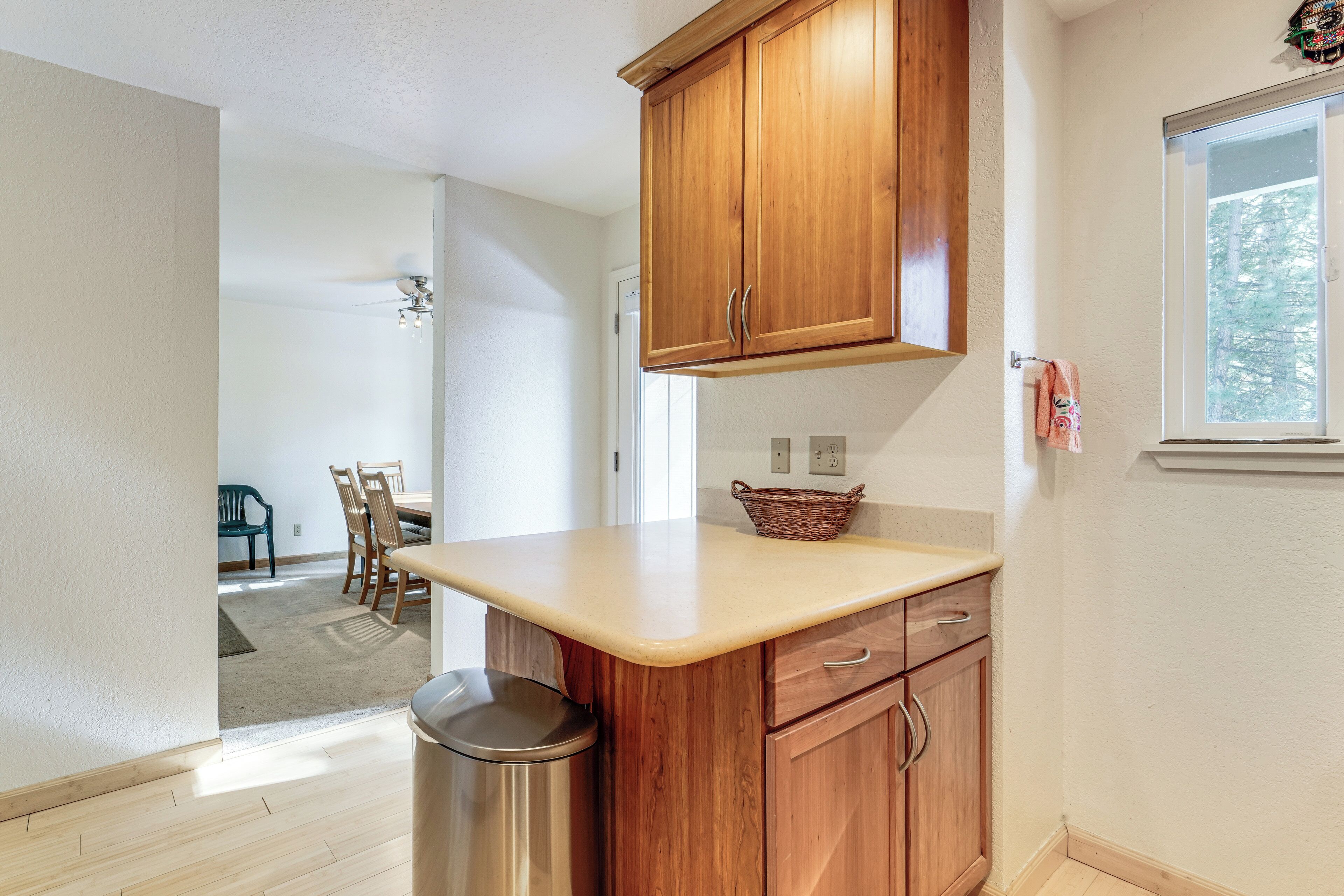 A kitchen with wooden cabinets, a countertop, and a trash can.